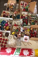 Multiple open boxes and trays with vintage glass Christmas ornaments in various colors such as blue, pink, red, gold, and green with vintage Santa and angel ornaments and miscellaneous small decor pieces.