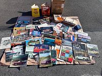 Wide view of full assortment of vintage automotive brochures and magazines laid out on ground, showing many colorful covers of classic American cars and automotive manuals