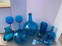 Full set of seven rich blue glass items displayed against white backdrop, showing varying shapes and two stemmed glasses with beads.
