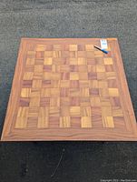 Top view of square wooden table displaying the checkered wood pattern on the top surface and a pen for scale.