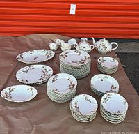 Full lot of Haviland H&C Limoges china with floral pattern including plates, bowls, cups, and platters arranged on brown paper outdoors.