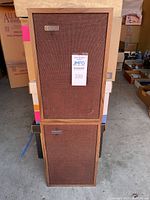 Front view of stacked pair of speakers showing wood cabinet and brown fabric grille with Scott badges