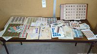 Overview of multiple albums and sheets of unused U.S. stamps spread on a table showing a variety of stamp designs and denominations.
