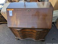 Front view of vintage walnut secretary desk with slant front and four drawers, showing wood grain and brass hardware.
