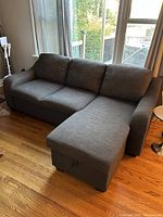 Grey fabric chaise sectional shown with upright chaise position against window and hardwood floor