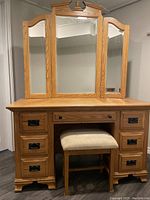 Full view of vanity and matching stool showing wood grain, drawer hardware and mirror panels.