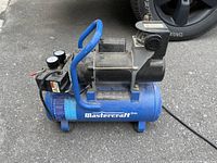 Front-side view of the blue Mastercraft air compressor showing tank, gauges, handle, and motor housing.