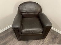 Front view of small brown leather club chair showing cushioned seat, back, and armrests.