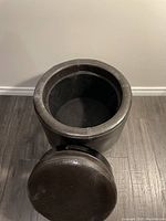 Top-down view of the storage ottoman showing open storage compartment and detached lid on the floor.