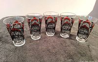Photo of six stained glass styled Coca Cola flair glasses arranged in a line showing front black and red floral and geometric artwork.