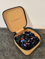 Open case showing mixed vintage marbles inside including black swirl, blue, red, and clear types.