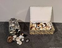 Lot of mixed vintage buttons spilled from a glass jar and placed next to a cardboard box filled with more buttons.