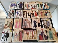 Wide view of entire lot showing 26 vintage sewing pattern envelopes laid out on floor surface, with diverse 1970s-80s garments on envelope covers.