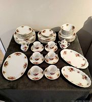 Full set arranged on dark cloth showing stacked plates, bowls, cups with saucers, cream, sugar bowl, and platters. Floral patterned china with no visible damage.