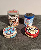 Four Planters Peanuts collectible tins overview showing different sizes, shapes, and colors on dark gray fabric