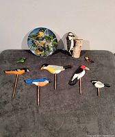 First image showing the complete assortment including the collectors plate, woodpecker sculpture, small ornaments, and seven garden bird stakes.