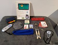 Full overview of assorted games including Target Pool boxed set, wooden Houdini puzzle, Pass The Pigs pouch, electronic game device, cards, discs, and game boards laid out on gray cloth surface.