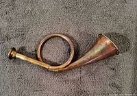 Full view of the vintage copper hunting horn showing the circular coil and mouthpiece side, highlighting the tarnished copper surface and the bell shape.