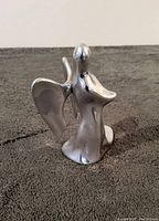 Front and left side view of the polished metal angel candle holder sculpture depicting the flowing robe, round head, and extended wide wings