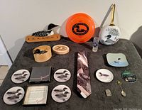 Full lot overview showing assorted loon-themed collectibles on black background including wooden carving, frisbee, tie, pins, plates, and coasters.