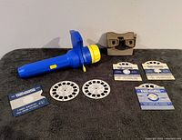 Vintage beige View-Master viewer and blue Super Show viewer with four reels on a grey cloth background