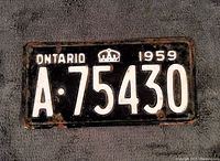 Front side of the vintage 1959 Ontario license plate showing the black background and white embossed characters 'A-75430', the white crown emblem, and the text 'Ontario 1959'. Some rust and paint wear present.