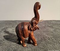 Front-side view of the vintage African elephant wooden sculpture showing raised trunk, tusks, and wood grain texture.