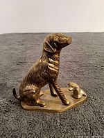 Front and side angle of vintage brass dog and puppy sculpture on textured surface.