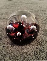 Side angle photo of the clear glass paperweight showing deep red internal design with clear protrusions and bubbles.