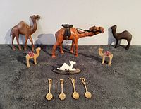 Lot of vintage camel figurines and four gold-plated spoons arranged on a flat dark surface.