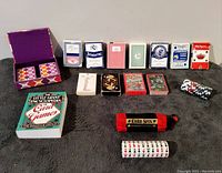 Photo showing the full assortment of seven playing card decks, poker chips, the Card Spin game, and the card games book spread out on a grey surface.
