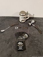 Lot arranged showing ceramic stein, brass bar tools, and deck of playing cards on grey surface.