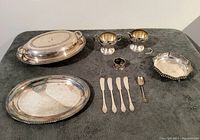 Front view of full set laid out on table showing all pieces including casserole with lid, trays, creamer, salt cellar, knives, spoon, and small basket