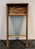 Full front view of vintage washboard showing wood frame, glass scrubbing panel and printed advertising text on top wood panel.