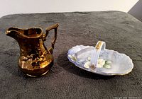 Wide view of the Wade lusterware pitcher and handpainted candy dish placed side by side on a dark fabric surface.