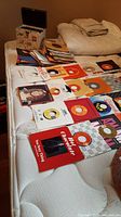 Photo showing a variety of vinyl 45 RPM records spread on a bed, with some records featuring visible labels and cover art.