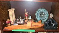 Shelf with wooden hand plane, black desk clock, decorative trivet plate, floral ceramic candle holders, and small bird figurines with feathers.