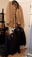 Three men's jackets hanging on a door: tan GAP jacket with buttons, black and navy jackets with zippers