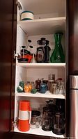 Photo showing shelves with four coffee presses, two decanters, tea mug strainer, measuring spoons, salt and pepper shakers, and thermoses.