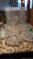 Photo showing multiple crystal pieces including covered dish, bowls, bottle holder, and candle holders arranged on countertop.
