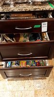 Photo showing three wooden drawers with various kitchen items inside, partially open.
