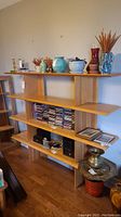 Full front view of wood display shelf with various decorative items on top and middle tiers, CDs on middle shelf, and other items below. Shelf shows light wear and tear.