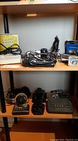 Photo of shelves showing various electronics including charger, alarm clock, Panasonic CD-ROM, Garmin device, and headphones.
