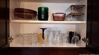 Top shelf showing two covered FireKing loaf pans, green and amber bowls, and Pyrex round casserole and loaf pan.