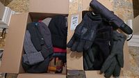 Two boxes containing multiple winter hats and gloves, hats are mainly knit and fabric, gloves vary in style and material.