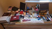 Wide view of all items laid out on a bed including photo albums, exercise books, binders, DVD writer, battery charger, staplers, and assorted office supplies.