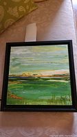 Framed original painting in a black frame showing a serene green landscape and yellow sky with painterly brushstrokes.