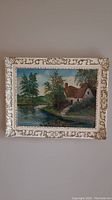 Full view of vintage framed painting showing a cottage by a pond, detailed white and gold ornamental frame.