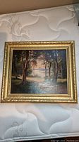 Full view of the framed original landscape oil painting showing forest, lake, and sky.