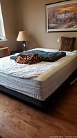 Queen size bed assembly with mattress, boxspring on black wheeled frame, and bedding including blanket, comforter, and pillows.